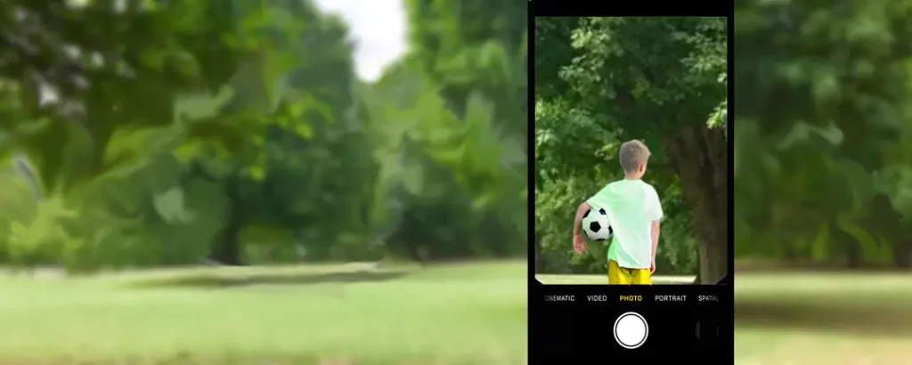 Kid facing away from you in the same park, green shirt, yellow shorts and a soccer ball under his arm. the boy is framed in a magnified cell phone screen. the park around him, not viewed thru the screen is blurry